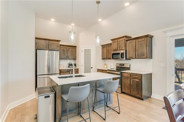 kitchen featuring appliances with stainless steel finishes, pendant lighting, sink, a center island with sink, and light hardwood / wood-style flooring