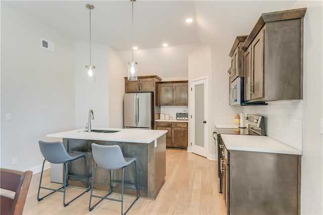 kitchen with an island with sink, sink, hanging light fixtures, light hardwood / wood-style floors, and stainless steel appliances