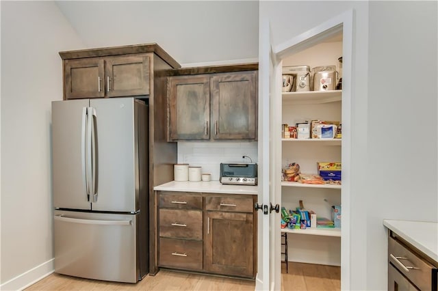 kitchen featuring tasteful backsplash, dark brown cabinets, stainless steel refrigerator, and light hardwood / wood-style floors