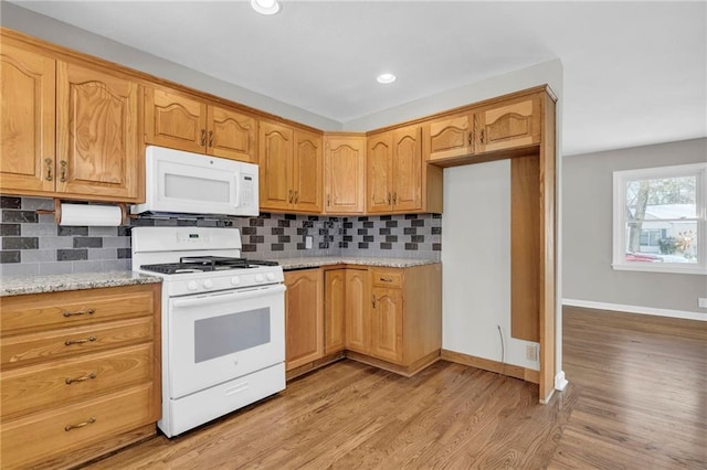 kitchen with tasteful backsplash, light stone countertops, white appliances, and light hardwood / wood-style floors