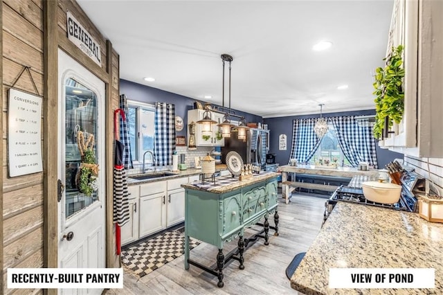 kitchen featuring sink, white cabinetry, light stone counters, a kitchen island, and decorative light fixtures