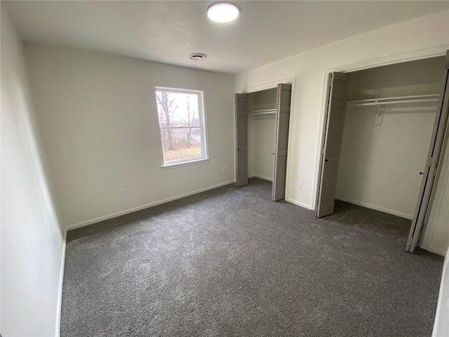 unfurnished bedroom featuring multiple closets and dark colored carpet