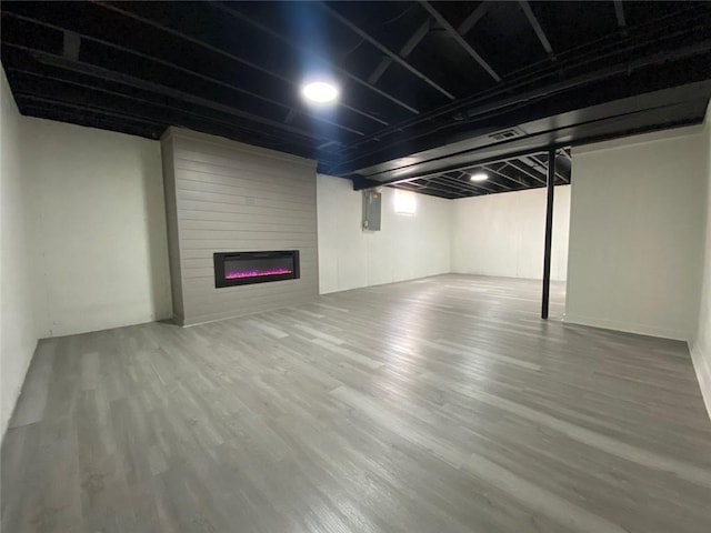 basement with wood-type flooring, electric panel, and a large fireplace