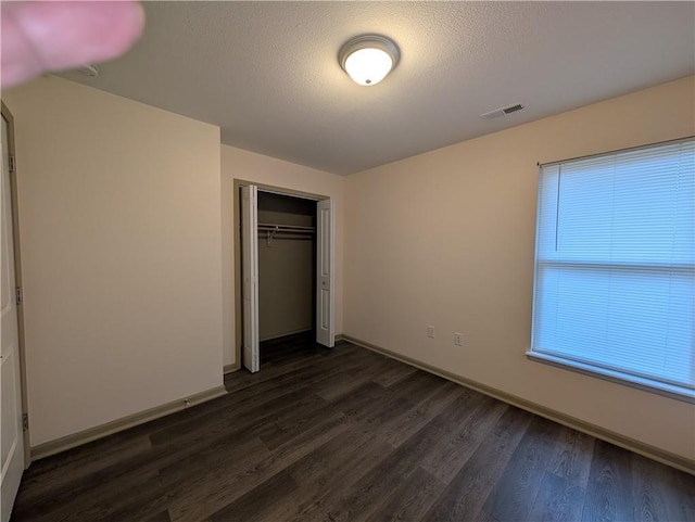 unfurnished bedroom with multiple windows, dark hardwood / wood-style flooring, a closet, and a textured ceiling