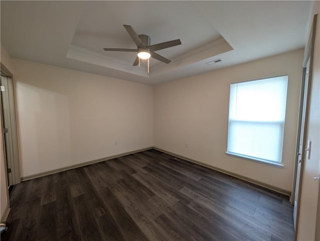 empty room with dark hardwood / wood-style floors, ceiling fan, and a tray ceiling