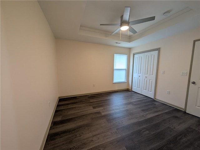 unfurnished bedroom with a closet, dark wood-type flooring, a raised ceiling, and ceiling fan