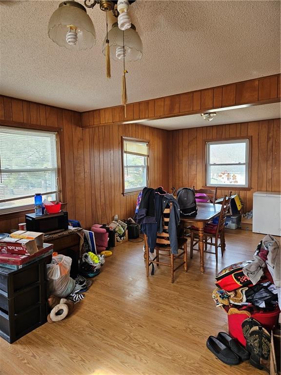 dining area with wooden walls, a textured ceiling, and light wood-type flooring