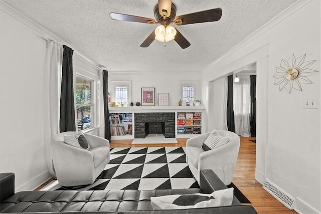 living room with crown molding, ceiling fan, hardwood / wood-style floors, a fireplace, and a textured ceiling