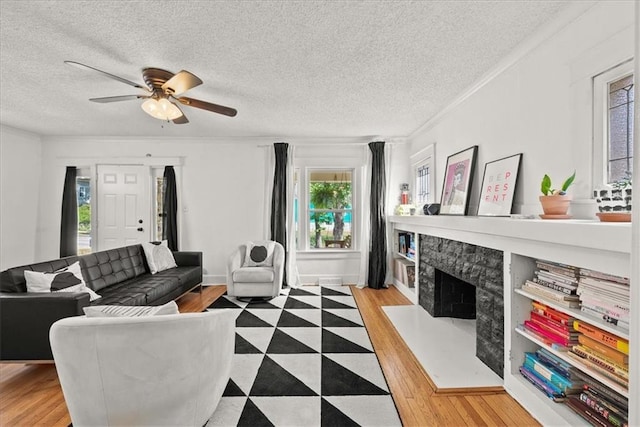 living room with crown molding, ceiling fan, a fireplace, a textured ceiling, and light wood-type flooring