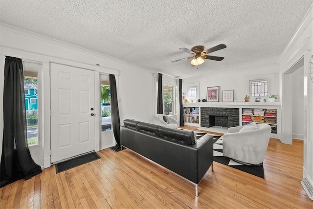 living room featuring light hardwood / wood-style flooring, a textured ceiling, ornamental molding, ceiling fan, and a fireplace