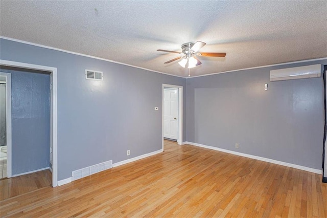 spare room featuring ceiling fan, a wall mounted AC, light hardwood / wood-style flooring, and a textured ceiling