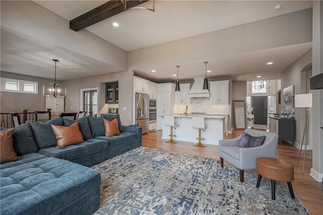 living room featuring an inviting chandelier, beam ceiling, sink, and light hardwood / wood-style flooring