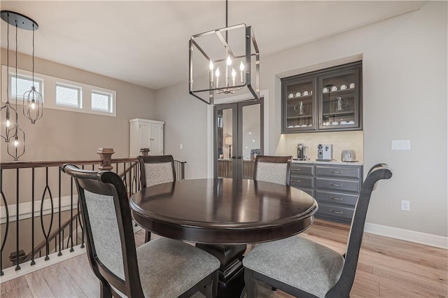 dining space with light wood-type flooring, an inviting chandelier, and french doors