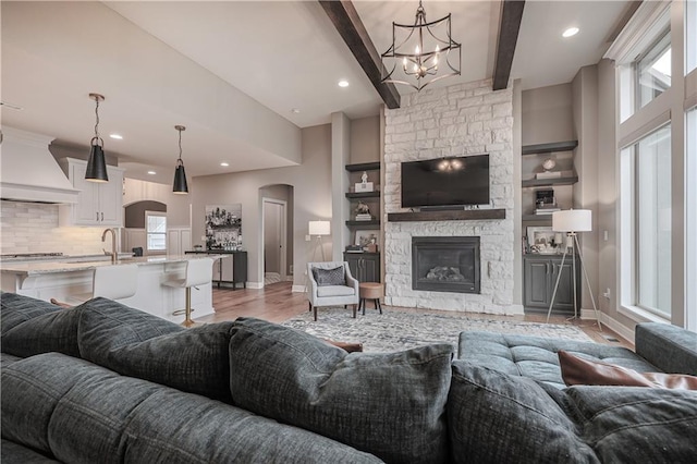 living room featuring beamed ceiling, a stone fireplace, a wealth of natural light, and light wood-type flooring