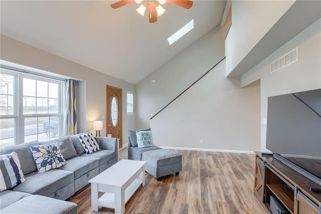 living room with hardwood / wood-style flooring, plenty of natural light, a skylight, and high vaulted ceiling