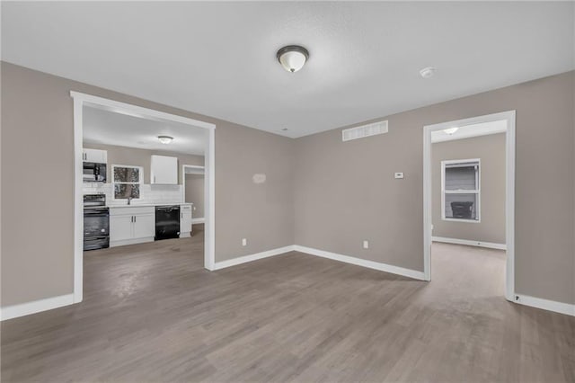 unfurnished living room featuring baseboards, visible vents, and wood finished floors