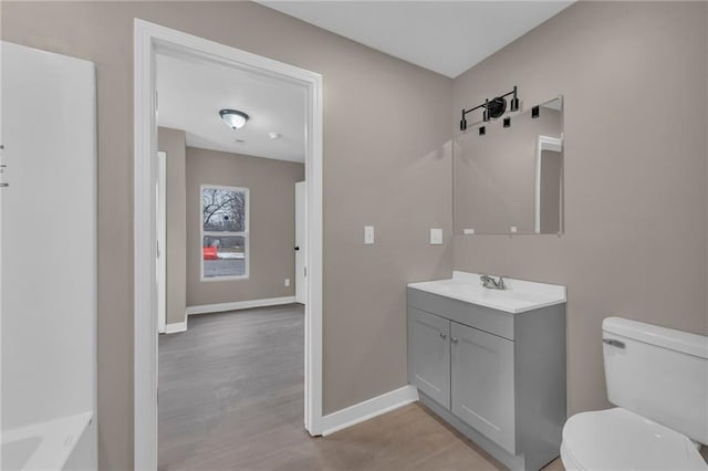 bathroom featuring toilet, baseboards, wood finished floors, and vanity