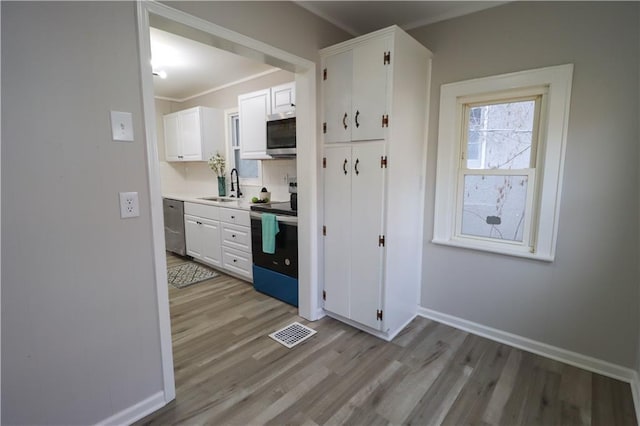 kitchen featuring appliances with stainless steel finishes, white cabinetry, sink, crown molding, and light wood-type flooring