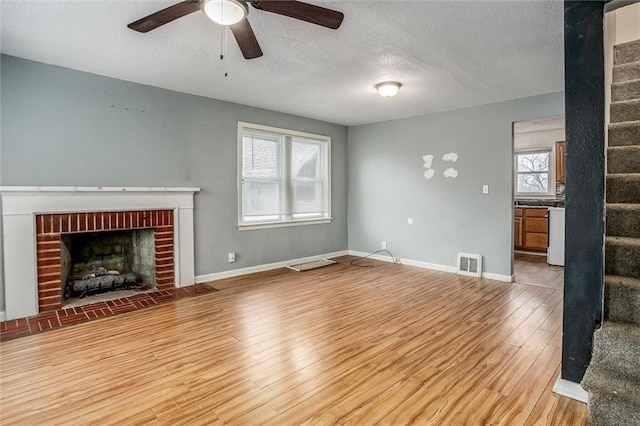 unfurnished living room featuring ceiling fan, a fireplace, light hardwood / wood-style floors, and a textured ceiling