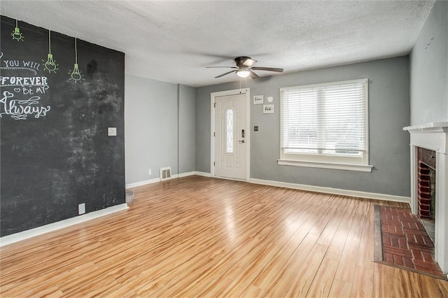 unfurnished living room with light hardwood / wood-style flooring, ceiling fan, a fireplace, and a textured ceiling