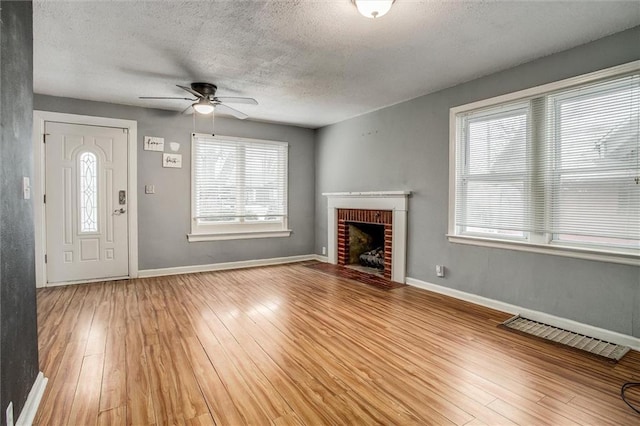 unfurnished living room with ceiling fan, a fireplace, light hardwood / wood-style floors, and a textured ceiling