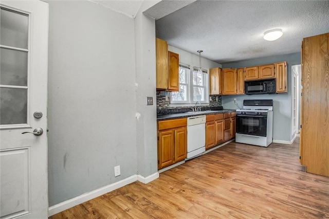 kitchen featuring sink, white appliances, hanging light fixtures, a textured ceiling, and light wood-type flooring