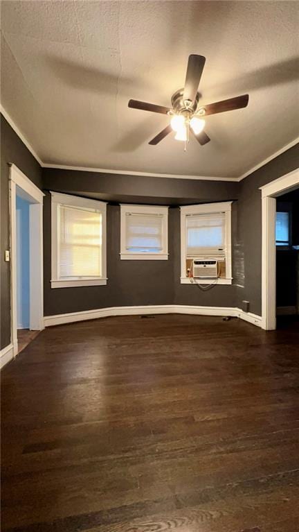 empty room featuring cooling unit, dark wood-style flooring, a ceiling fan, baseboards, and ornamental molding