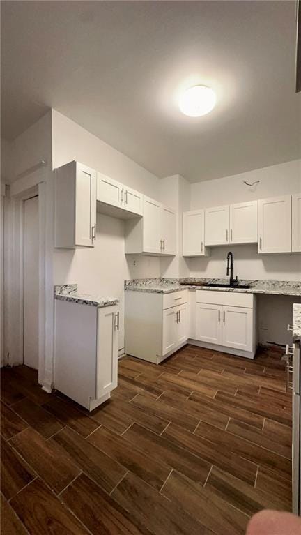 kitchen featuring wood finish floors, white cabinets, a sink, and light stone countertops