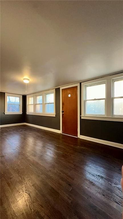 unfurnished living room featuring dark wood-type flooring and baseboards