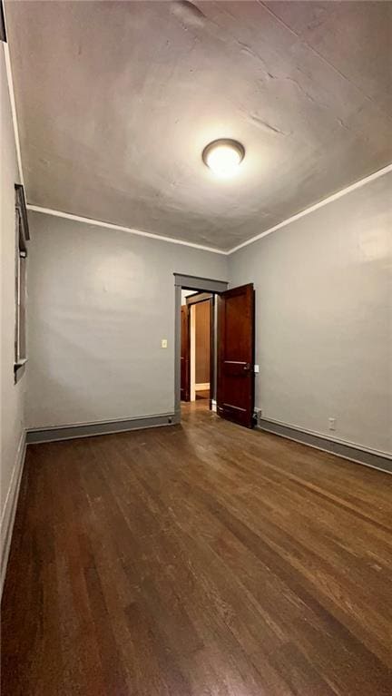 unfurnished room with dark wood-style floors, baseboards, and crown molding