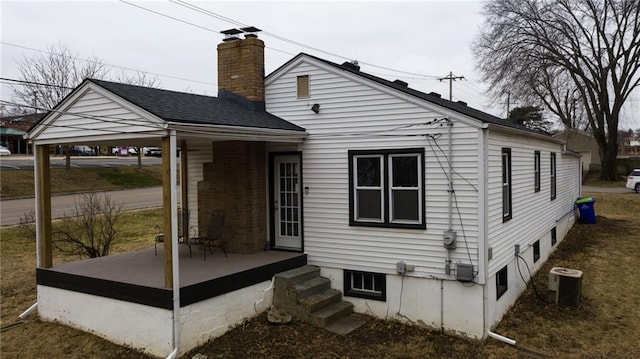 back of house featuring roof with shingles, a chimney, and central AC unit