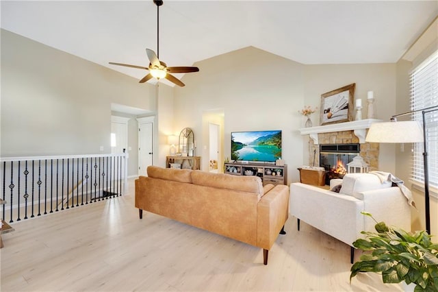 living room featuring ceiling fan, high vaulted ceiling, a stone fireplace, and light hardwood / wood-style floors