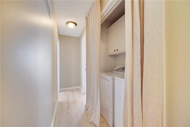 washroom with cabinets, a textured ceiling, washer and clothes dryer, and light hardwood / wood-style flooring