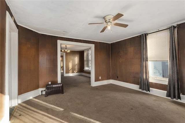 carpeted spare room featuring ornamental molding, ceiling fan with notable chandelier, and wood walls