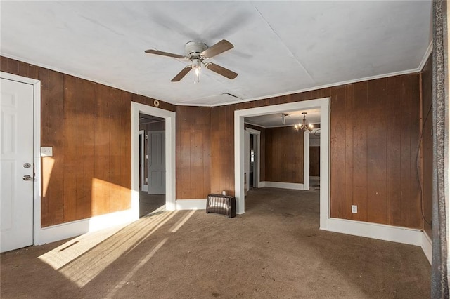 carpeted empty room featuring ceiling fan with notable chandelier and wood walls