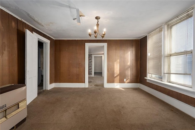 carpeted spare room with crown molding, wooden walls, and an inviting chandelier