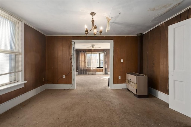 carpeted empty room with ornamental molding, a notable chandelier, and wood walls