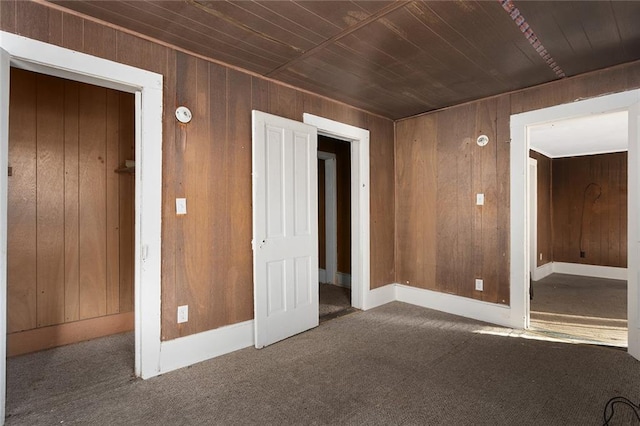 empty room featuring wood ceiling, dark carpet, and wood walls