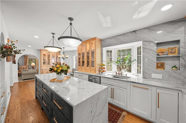 kitchen with hanging light fixtures, a center island, stainless steel dishwasher, light stone countertops, and light hardwood / wood-style flooring