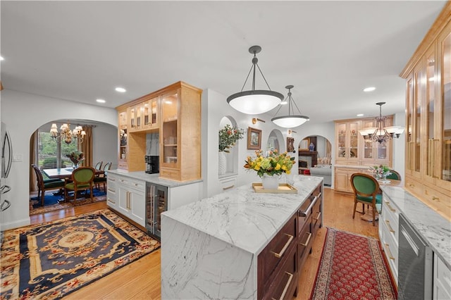 kitchen with an inviting chandelier, light stone counters, a center island, pendant lighting, and beverage cooler