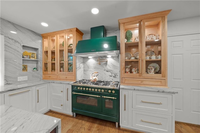 kitchen featuring wall chimney range hood, double oven range, tasteful backsplash, light hardwood / wood-style floors, and white cabinets