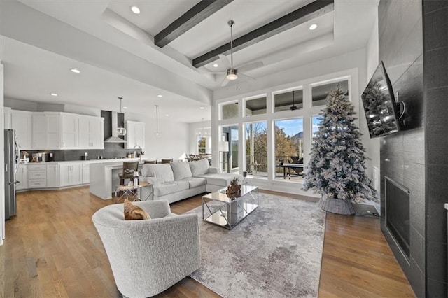 living room featuring light hardwood / wood-style flooring, ceiling fan, beam ceiling, a towering ceiling, and a fireplace