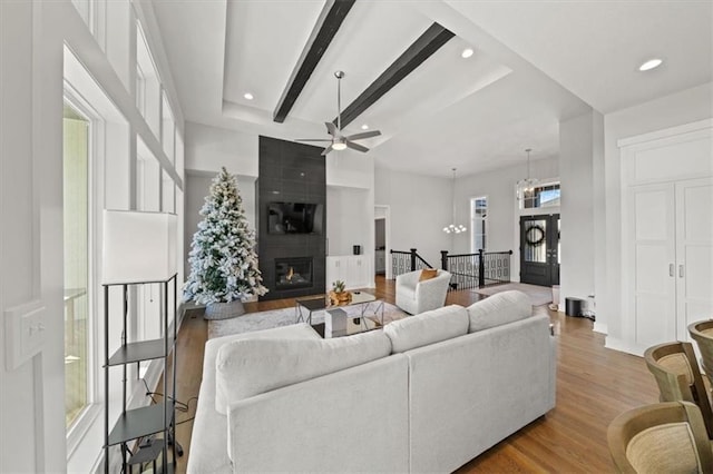 living room featuring ceiling fan with notable chandelier, light hardwood / wood-style flooring, a large fireplace, and beamed ceiling