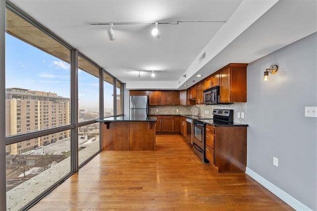 kitchen with dark countertops, light wood finished floors, backsplash, floor to ceiling windows, and appliances with stainless steel finishes