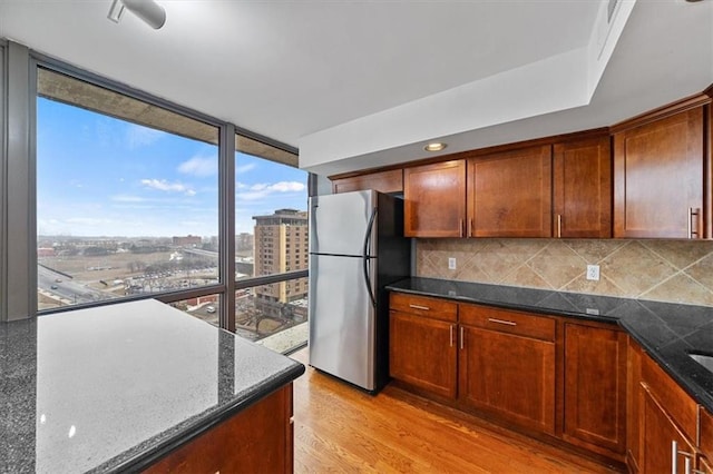 kitchen with a wall of windows, dark stone countertops, freestanding refrigerator, decorative backsplash, and light wood-type flooring