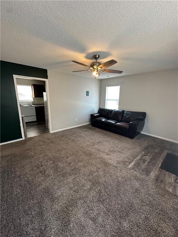 living room featuring a textured ceiling, ceiling fan, and dark colored carpet