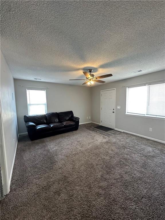 unfurnished living room featuring dark colored carpet, plenty of natural light, a textured ceiling, and ceiling fan