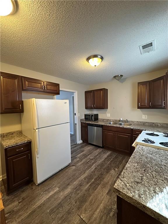 kitchen with dark brown cabinetry, sink, white appliances, and dark hardwood / wood-style floors