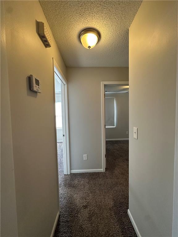 hallway with a textured ceiling and dark colored carpet