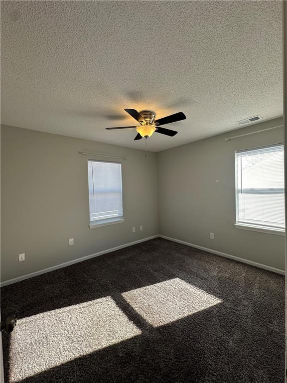 empty room featuring ceiling fan, a textured ceiling, and dark carpet